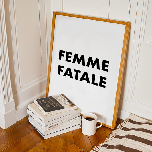 Framed poster with 'Femme Fatale' text on a stack of books and a mug on a wooden floor.